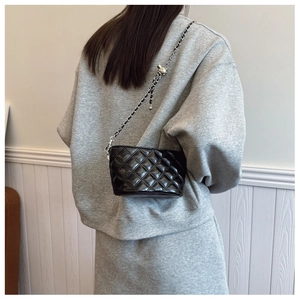 Detail of black quilted chain bag with a silver ball slider buckle on shoulder strap