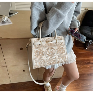 Detail of embroidered floral pattern on beige crossbody bag held by a model in a warm setting
