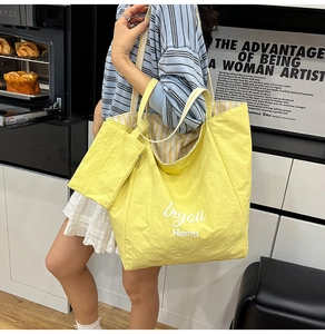 Detail view of a large yellow nylon tote bag with inner striped lining and small pouch