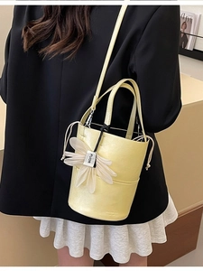 Minimalist light yellow bucket bag with a white flower charm and adjustable strap