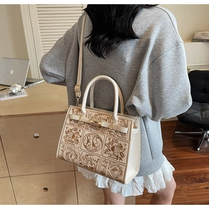 Detail view of beige embossed handbag showing intricate floral patterns and top handles
