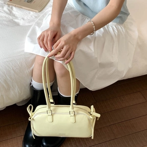 Detail of a creamy yellow glossy faux leather baguette bag with side bow accents