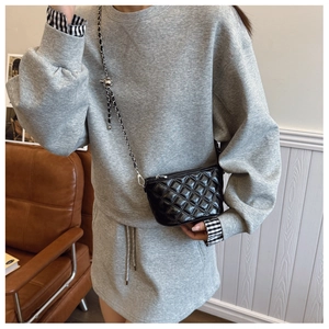 Detail of black quilted crossbody bag with silver chain strap shown in home setting
