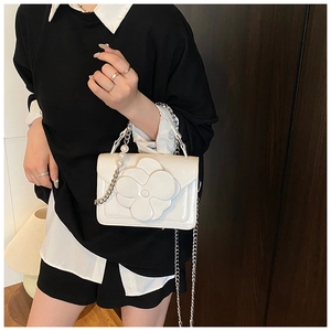 Detail of white mini crossbody bag featuring a large 3D flower and pearl handle strap