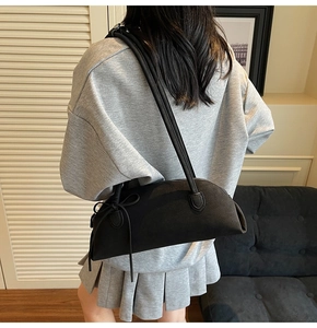 Detail view of black crescent shoulder bag with bow decor on a model in a minimalist room