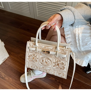 Detail of embroidered beige tote bag with golden lock and delicate patterns