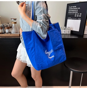 Close-up of blue nylon tote bag with white lettering and striped lining on shoulder
