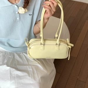 Detail of a yellow faux leather baguette bag with side bow and brand engraving