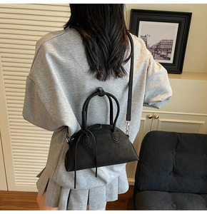 Detailed view of a black Boston shell bag worn crossbody by a model in a cozy home setting