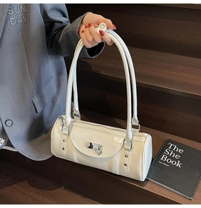 Detail view of a white cylindrical handbag with silver heart charm on wooden background