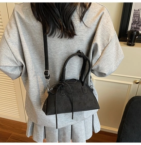 Model view of black pebbled leather bow handbag with cylindrical handles and crossbody strap