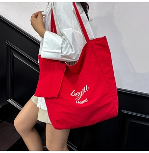 Detail of red nylon tote bag with artistic lettering and matching mini pouch on a model