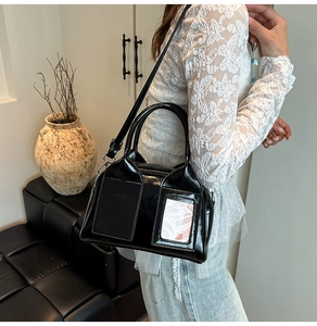 Detail of a black glossy patent leather Boston bag styled in a minimalist interior setting