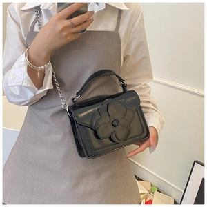 Detail of elegant black leather crossbody bag featuring a large 3D flower and silver chain