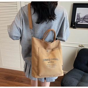 Back view of a khaki canvas tote bag worn as a shoulder bag in a cozy indoor setting