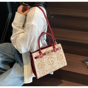 Detailed close-up of embroidered Boston bag with red leather handles and gold lock buckle