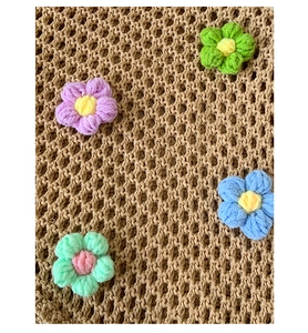 Close-up of hand-woven mesh beach tote featuring 3D colorful crochet floral details