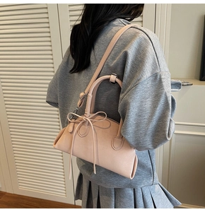 Detail of light pink pebble leather shell bag with bow ribbon on grey model outfit