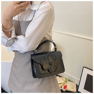 Detail of black patent leather crossbody bag featuring a large camellia flower and chain strap