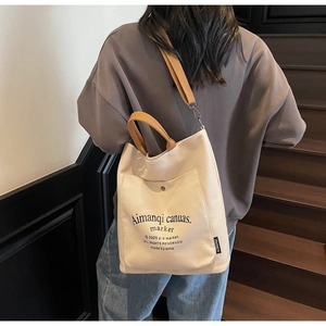 Detail of minimalist off-white canvas tote bag with brown straps worn on shoulder