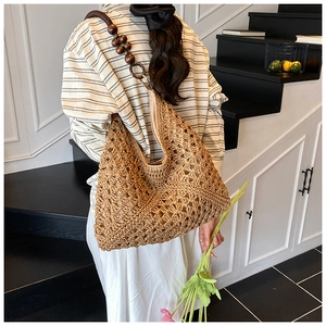 Close-up of woven straw tote bag with unique dark wooden bead shoulder strap detail