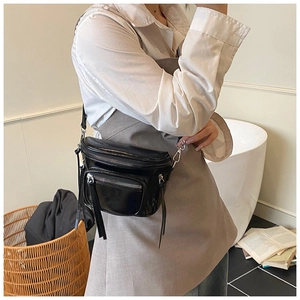 Détail d'un sac bandoulière en cuir noir brillant avec zips argentés porté par un mannequin