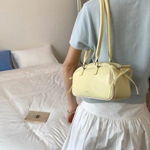 Pale yellow patent leather baguette bag with side bows shown in a lifestyle setting