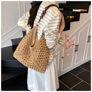 Close-up of woven straw tote bag with wooden bead straps on a model's shoulder