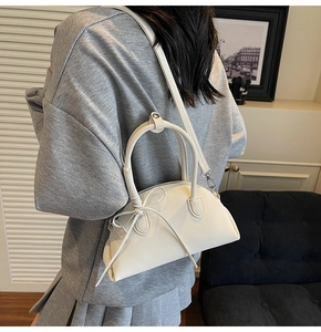 Detail showing the white pebbled leather texture and decorative bow on the shell handbag