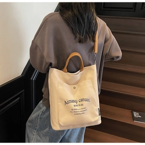 Close-up of beige canvas tote bag with brown leather handles and adjustable shoulder strap