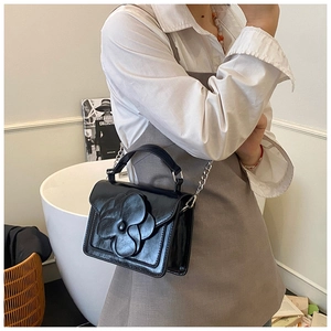 Detailed view of the 3D flower decoration on a black leather handbag with silver chain
