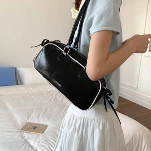 Detail showing glossy black faux leather texture with white piping and ribbon on a hobo bag