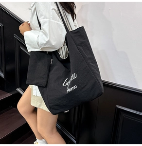 Detail view of large black nylon tote bag featuring aesthetic white text and small pouch