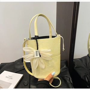 Detail of light yellow bucket bag with lychee texture and a large white flower charm