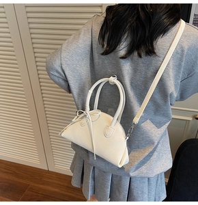 Detail of white half-moon bag with bow decoration and metal buckle strap on a model