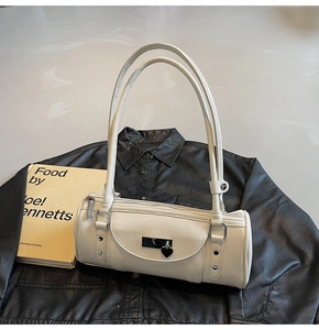 Detail of cream white cylinder bag with silver heart pendant and metal studs on leather background
