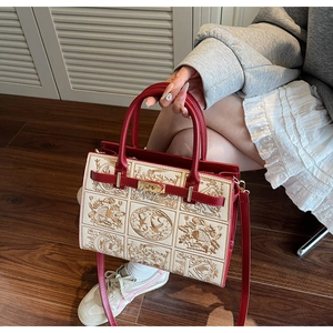 Detail of embroidered tote bag with red leather trim and golden twist lock closure