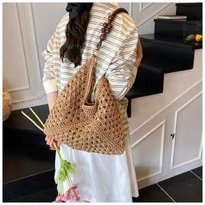 Detail of woven straw tote bag featuring decorative dark wood beads on shoulder strap