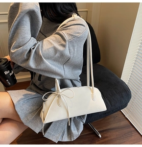 Chic white leather baguette shoulder bag with decorative bow ties shown on model