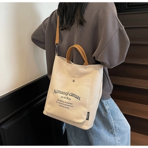 Detail of a cream canvas tote bag featuring brown straps and an outer pocket with a buckle