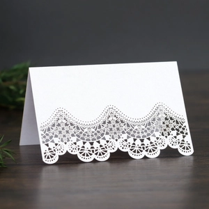 Laser-cut white wedding place card with intricate lace pattern on a wooden table