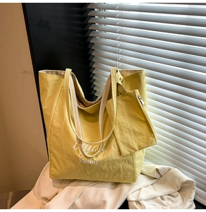 Detail of yellow tote bag with striped handles and matching small pouch on white fabric