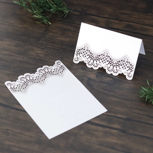 Close-up of white laser-cut lace place cards with intricate hollow design on wood