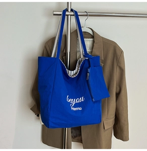 Detail of blue tote bag showing logo print, striped strap, and matching inner pouch