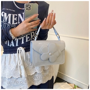 Detail shot of a light blue small flap bag featuring a large 3D floral applique decoration