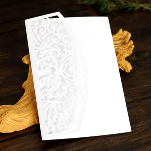 Detail of white laser-cut invitation card with intricate vine patterns on wood
