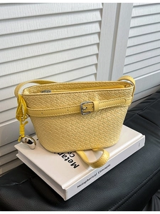 Borsa a secchiello intrecciata gialla con ciondolo a cuore su libro bianco e sfondo in pelle