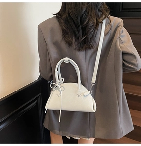 Detail of off-white half-moon crossbody bag with bow ribbon on a textured leather finish