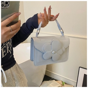 Close-up of a light blue square handbag with a 3D floral accent and top handle