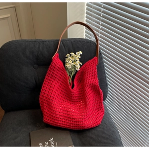 Detail of red hollow crochet knit tote bag with brown leather handles on a black chair